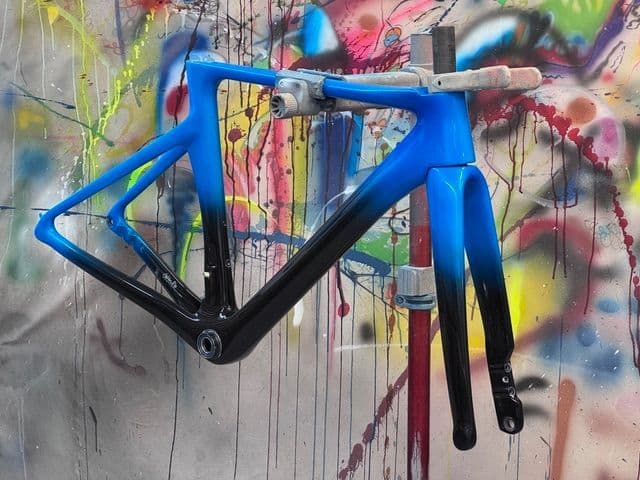 Frame finished with a fade from blue to black, photographed against the shop's paint-splattered backdrop.