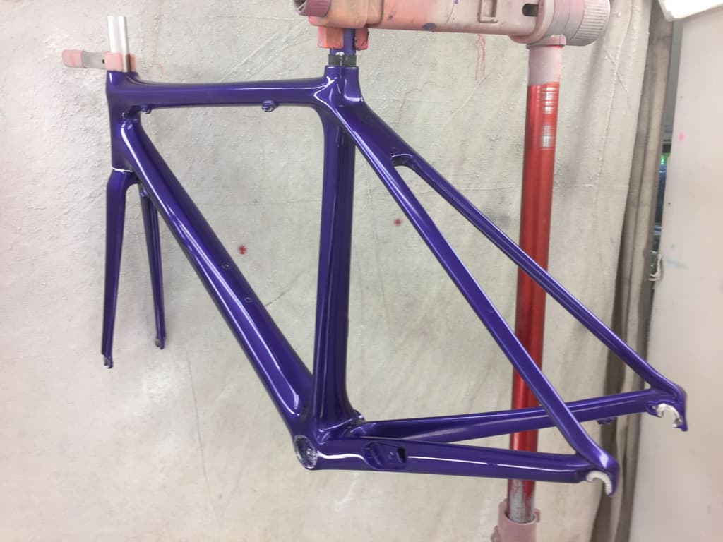 Rim-brake road frame finished in a deep gloss purple single-color paint job, photographed in the spray booth.
