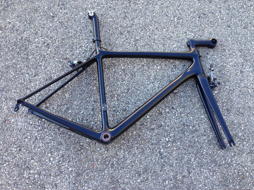 Unbranded road frame refinished in a plain matte black, photographed on pavement outside the shop.
