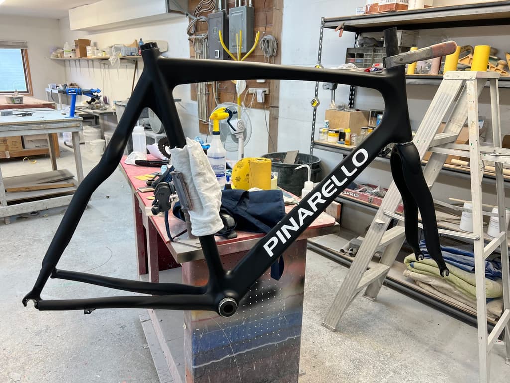 Pinarello road frame refinished in a satin black, shown on the shop workbench with reproduced white logo lettering.