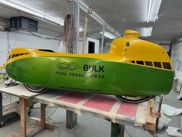 Velomobile fairing shell refinished in green and yellow — a cosmetic refinish rather than a bicycle frame.